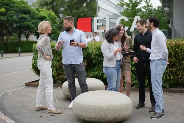 Group of professionals chatting outdoors, with a partial view of a large ELCA sign