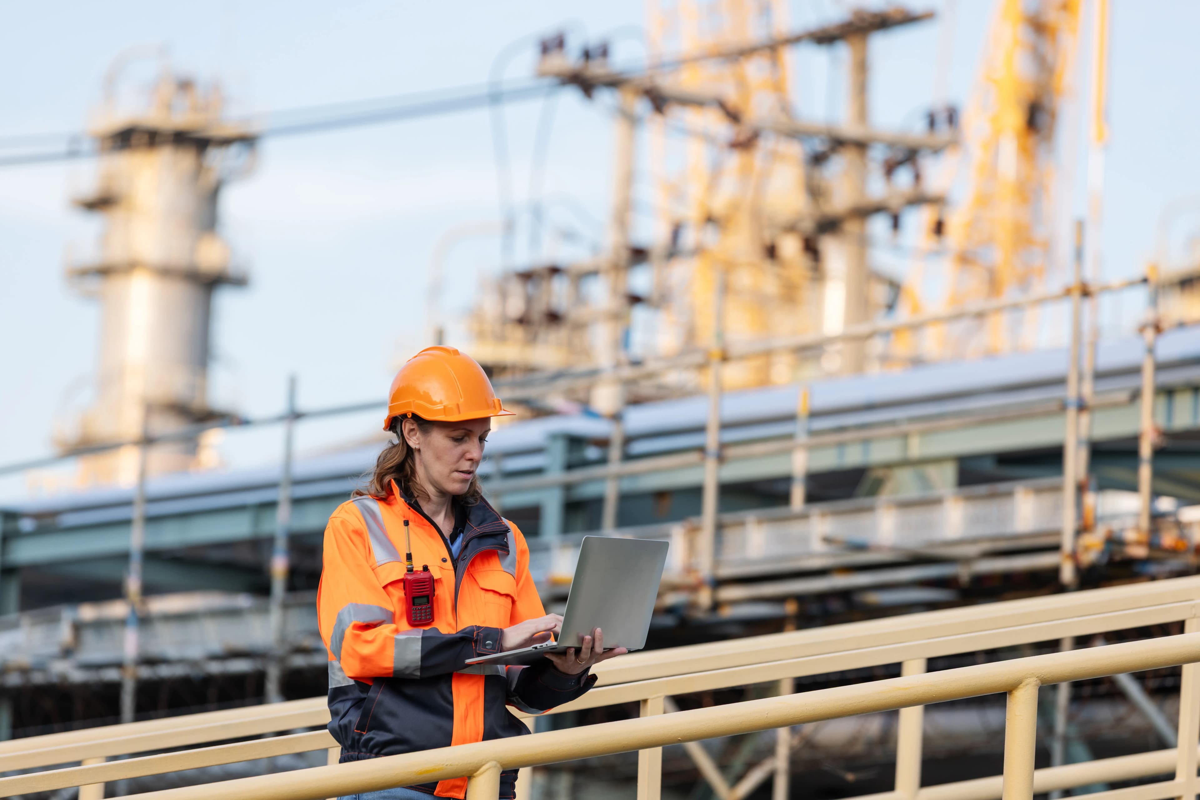 Engineer using a laptop at an industrial site, symbolizing automated software factory pipelines, CI/CD deployment workflows, and DevOps infrastructure automation