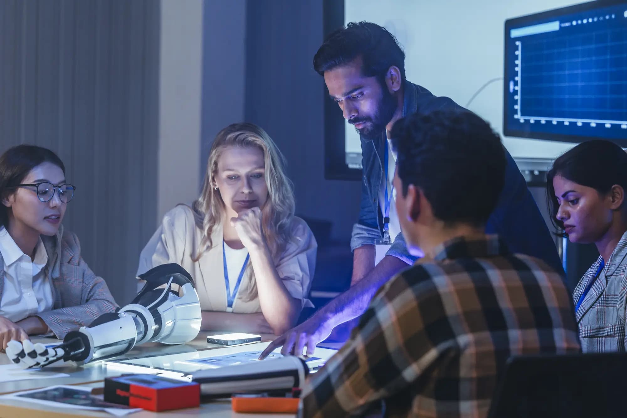 Technology team collaborating around a robotics prototype and digital interface, representing software delivery engagement models and collaborative engineering development.