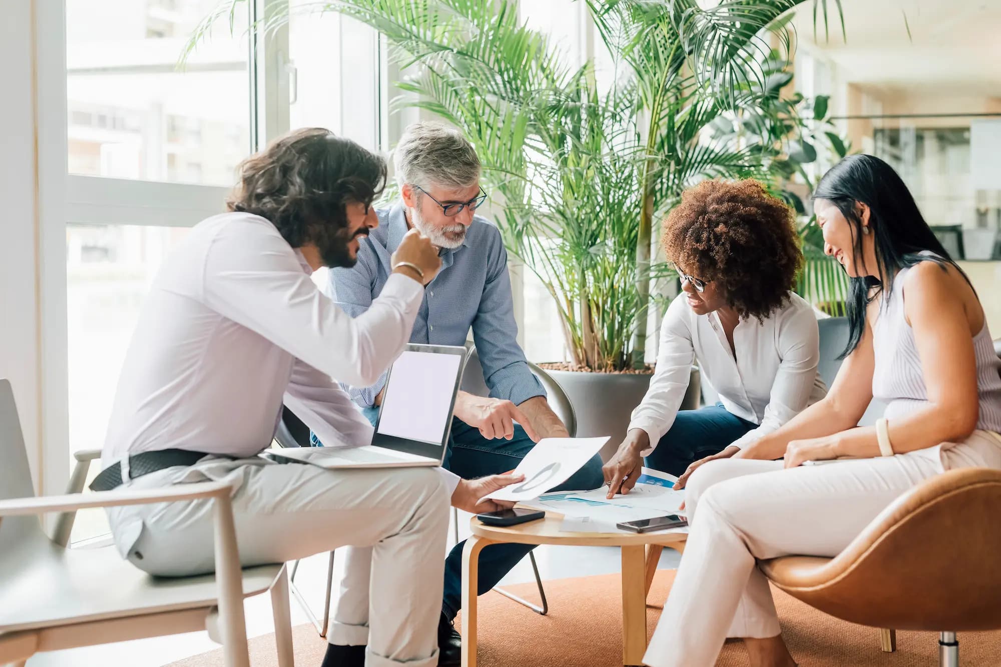 Business team collaborating in a modern office meeting, reviewing data and analytics on documents and laptop, illustrating corporate teamwork, digital transformation, and strategic consulting.