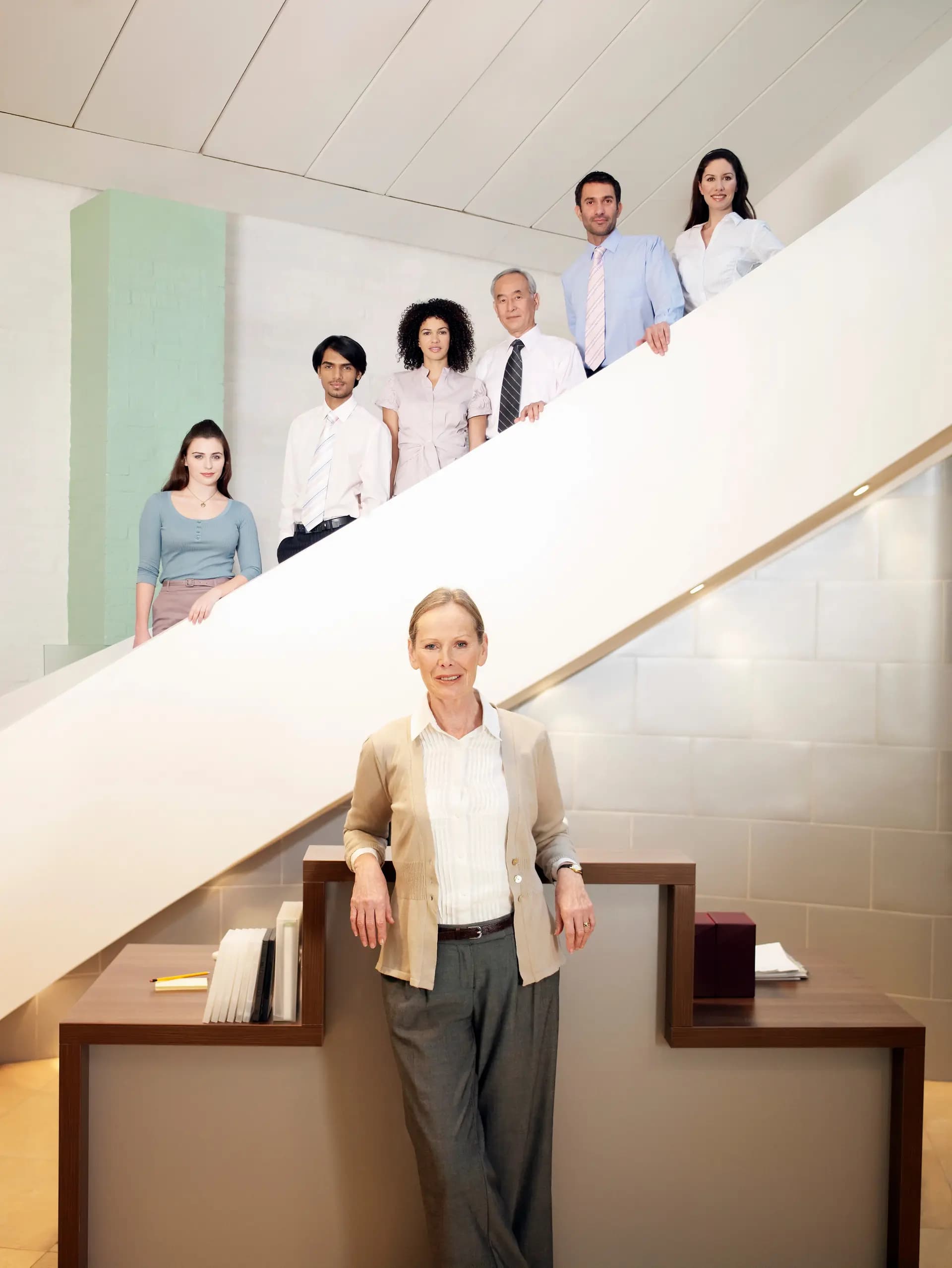 Professional team of diverse office employees standing on a modern staircase in a corporate workspace, representing collaboration, leadership, and workplace diversity in a contemporary business environment.